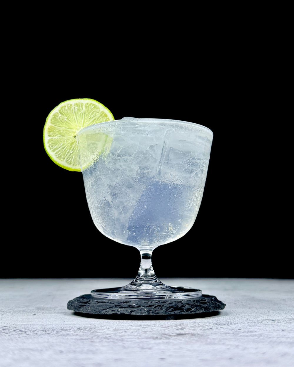 Margarita with a lime wheel in a stemmed glass on a dark stone coaster.